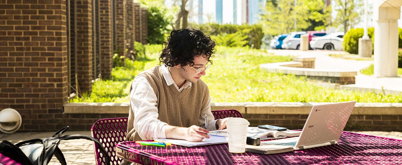 Student sitting outside with laptop taking notes and studying