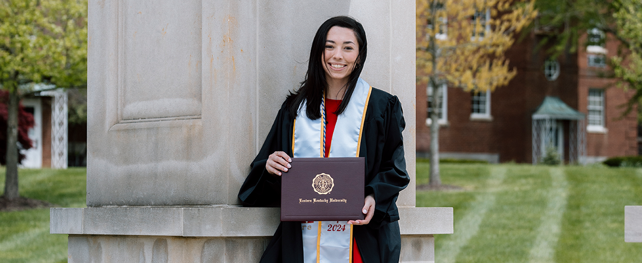 EKU graduate, Emma Thomas, holds her degree while wearing her graduation regalia