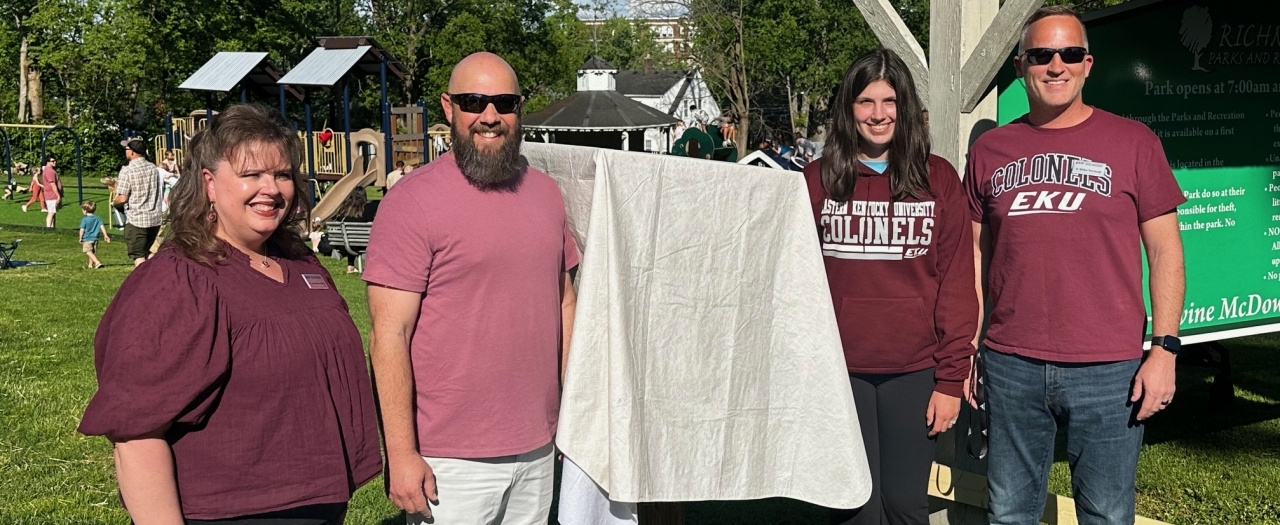 Contributors stand next to covered box at Unveiling of Little Free Library.